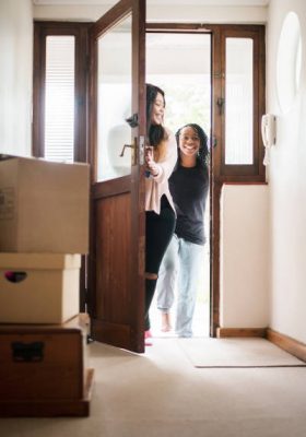 Shot of two young women entering from the main door of their new home